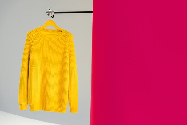 knitted yellow sweater on hanger on pink and grey background - Φωτογραφία, εικόνα