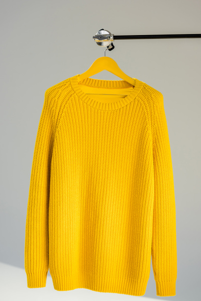 Gestrickter gelber Pullover auf Kleiderbügel vor grauem Hintergrund - Foto, Bild