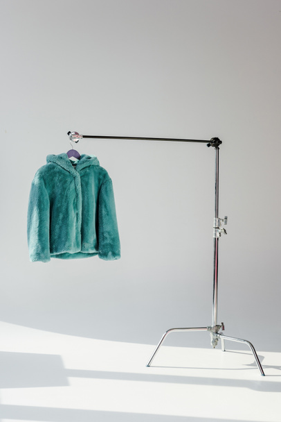 casaco de pele de falso verde macio pendurado no rack no fundo cinza
 - Foto, Imagem