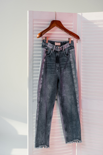 primer plano de jeans colgando en divisor de habitación blanca con rayos de sol
 - Foto, Imagen