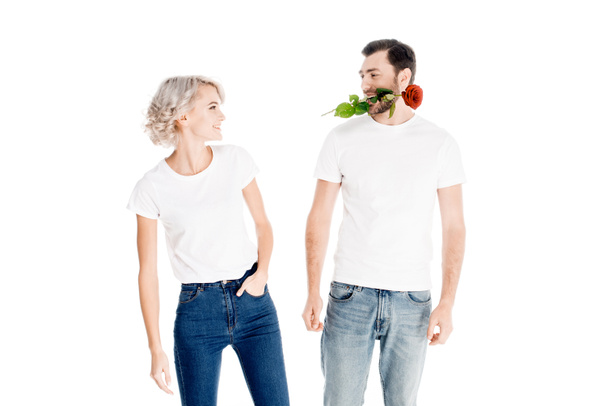 Belo casal olhando um para o outro, enquanto o homem segurando flor na boca isolado no branco
  - Foto, Imagem