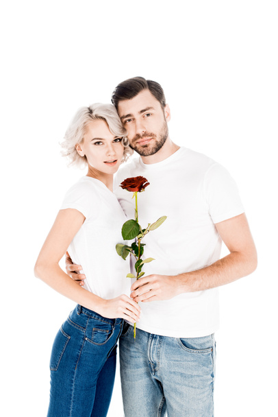 Όμορφο ζευγάρι με λουλούδι αγκάλιασμα ενώ κοιτάζοντας τα φωτογραφικών μηχανών που απομονώνονται σε λευκό  - Φωτογραφία, εικόνα