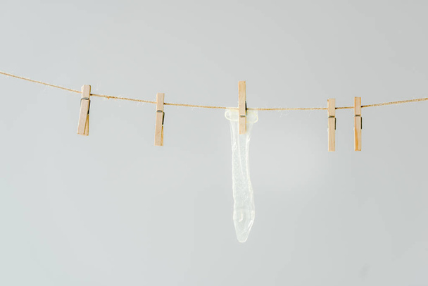 raw of wooden clothespins with white condom hanging on clothesline isolated on grey - Photo, Image