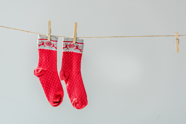 Nahaufnahme von roten festlichen Wintersocken, die an der Wäscheleine hängen, mit Wäscheklammern isoliert auf grau - Foto, Bild