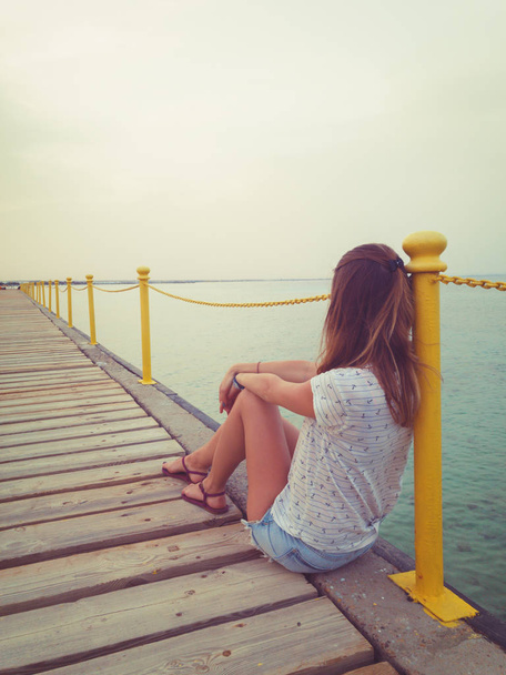 Girl sitting on a wooden pier and looking at the ocean. - Fotografie, Obrázek