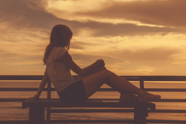 Silhoutte d'une fille assise sur un banc et regardant le paysage océan / mer
. - Photo, image