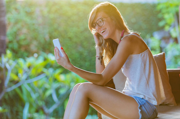 Милая девушка держит мобильный телефон и наслаждается летом
. - Фото, изображение