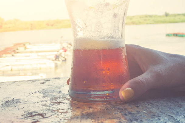 Dívka drží vychlazené pivo ve sklenici poblíž řeky s lodí. - Fotografie, Obrázek