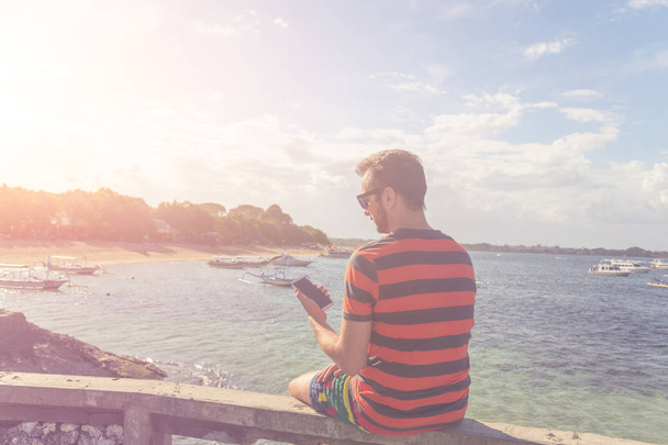 Hombre usando celular en la orilla del océano
. - Foto, Imagen