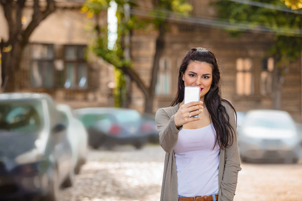 Nette junge Frau nutzt Handy in urbaner Umgebung. - Foto, Bild
