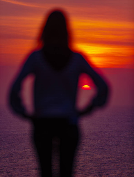 Mädchen genießt Sonnenuntergang / Sonnenaufgang von einer hohen Klippe über dem Wasser. - Foto, Bild
