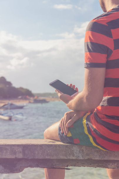 Man using cellphone on the ocean shore. - 写真・画像
