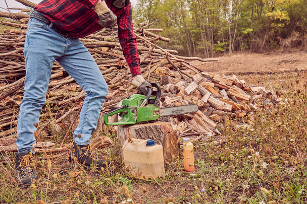 Lumberjack with chainsaw and pile of cut woods. - Foto, Imagen