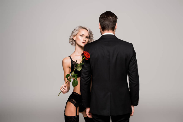 Seductive woman in lingeriewith red rose near man in black costume isolated on grey  - Foto, Imagem