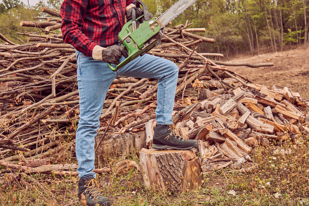 Lumberjack with chainsaw and pile of cut woods. - Foto, Imagen