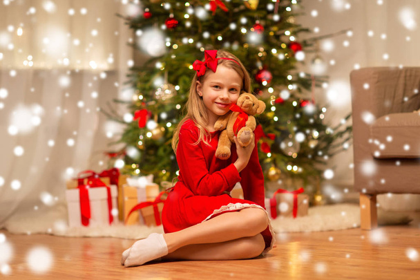 κορίτσι με κόκκινο φόρεμα που αγκαλιάζει το αρκουδάκι στο σπίτι - Φωτογραφία, εικόνα