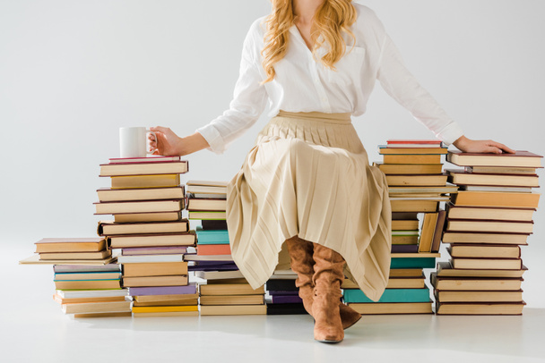 primer plano de la mujer adulta sentada en un montón de libros con taza
 - Foto, Imagen