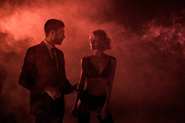 schönes Paar, das sich auf rotem Rauch-Hintergrund amourös ansieht - Foto, Bild