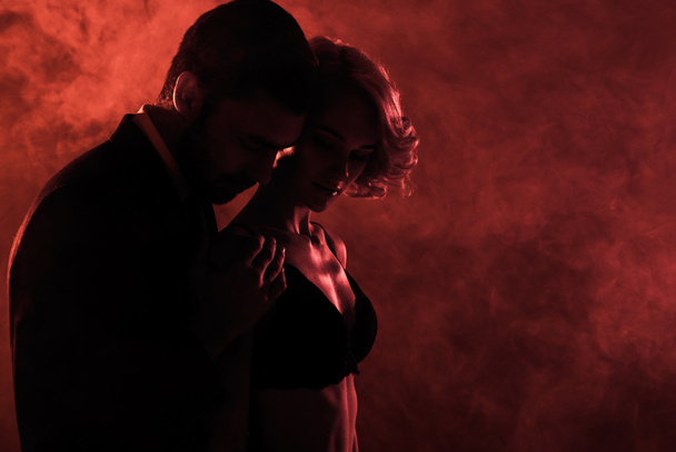 Mann zärtlich umarmt schöne Frau auf rotem Rauch Hintergrund  - Foto, Bild