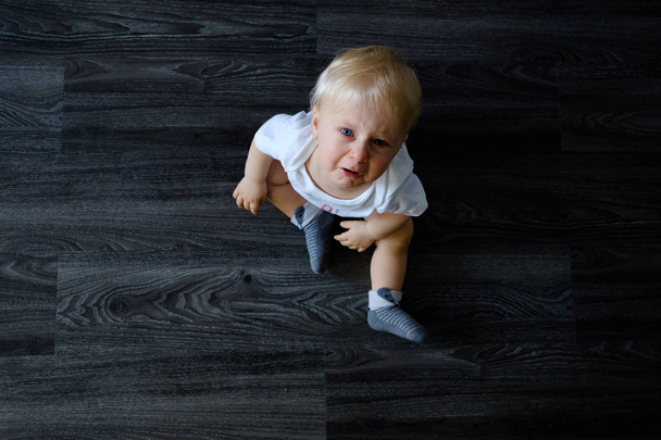 Upset baby in white bodysuit on the floor at home - Foto, imagen