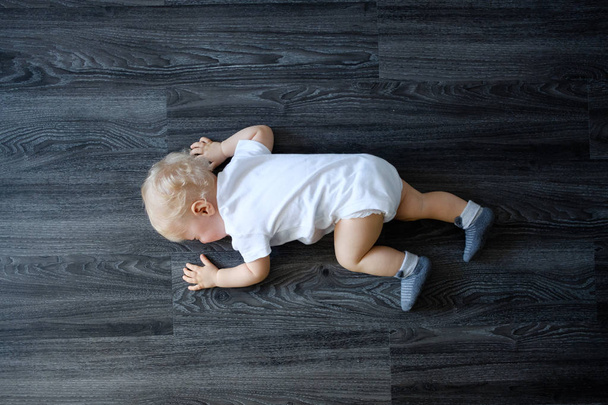 Upset baby in white bodysuit on the floor at home - Fotó, kép