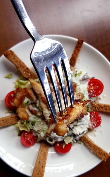 Cézár saláta fehér tányérra villával, levágott megtekintése. - Fotó, kép