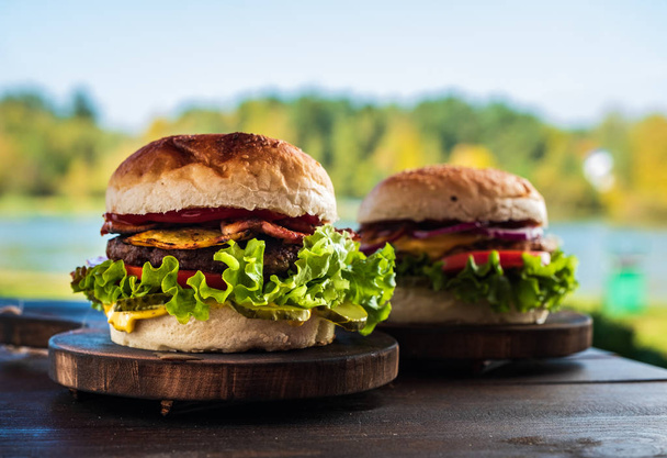 Lédús, ízletes sajtburger marha, saláta, savanyúság, paradicsom és hagyma karikákkal egy fából készült asztal. Klasszikus utcai élelmiszer - grillezett burger. - Fotó, kép