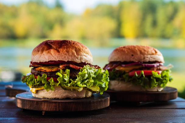 Lédús, ízletes sajtburger marha, saláta, savanyúság, paradicsom és hagyma karikákkal egy fából készült asztal. Klasszikus utcai élelmiszer - grillezett burger. - Fotó, kép