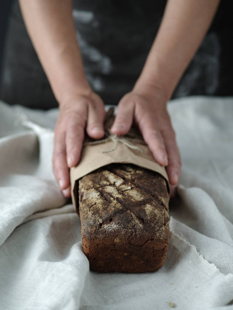 Руки женщины держат ржаной хлеб на темном фоне
 - Фото, изображение