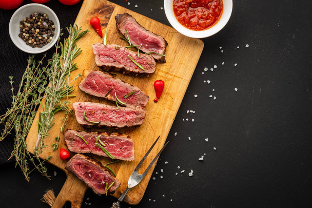 Slices of beef steak on meat fork on wooden cutting board - Photo, image