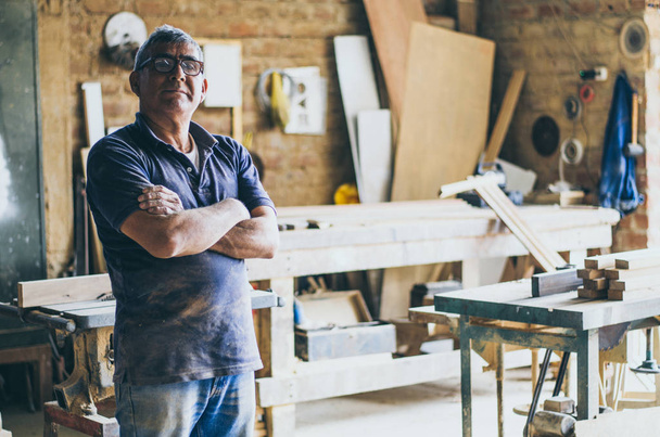 Portrait of senior carpenter in his workshop and looking at camera. - Photo, Image
