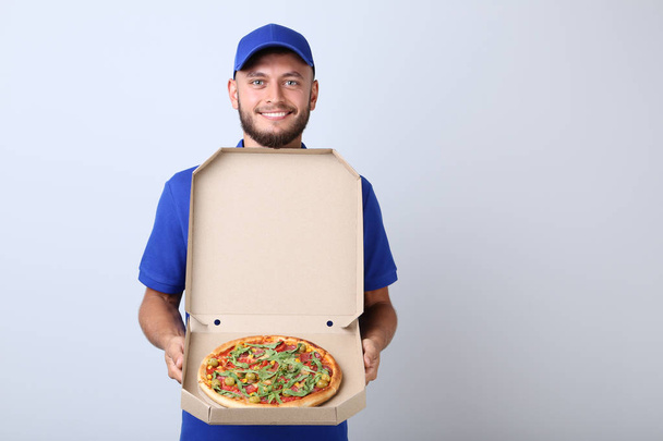 Delivery man with pizza in cardboard box on grey background - Fotoğraf, Görsel