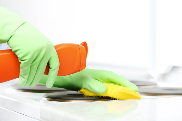 Hands in gloves with sponge and bottle of detergent cleaning electric stove - 写真・画像