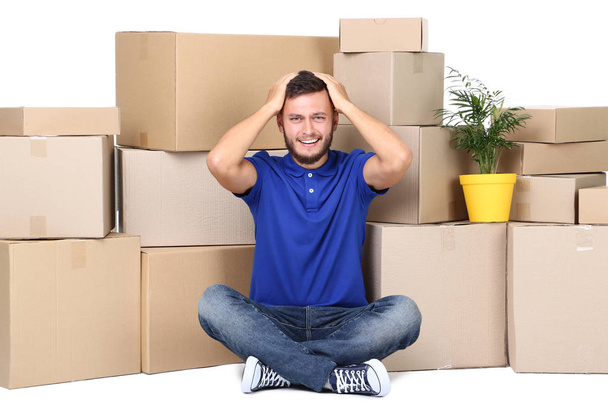 Young man with cardboard boxes and green plant on white background - Фото, изображение