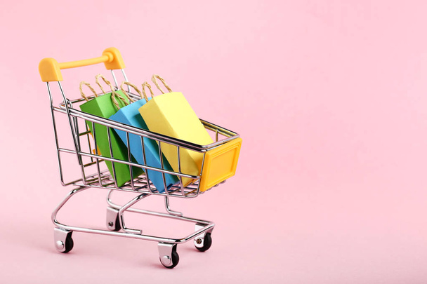 Small paper shopping bags with shopping cart on pink background - Fotografie, Obrázek