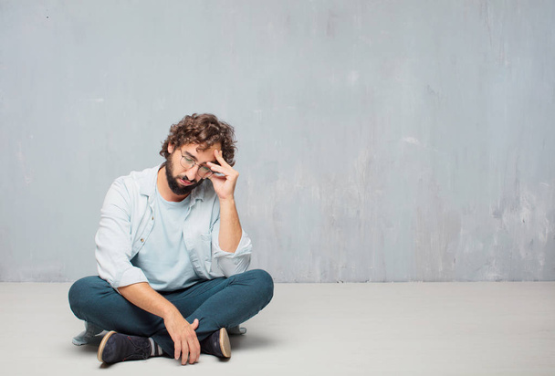Young cool bearded man sitting on the floor. Grunge wall background. - 写真・画像