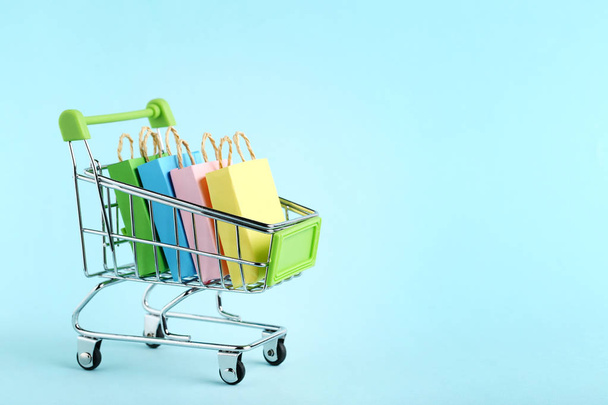 Small paper shopping bags with shopping cart on blue background - Photo, Image