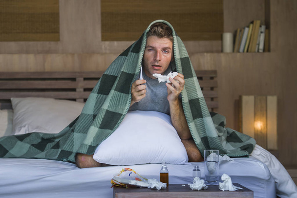 young sick wasted and exhausted man at home bed lying feeling unwell suffering cold and flu sneezing nose with tissues having virus and headache in domestic health care and grippe concept - Фото, изображение