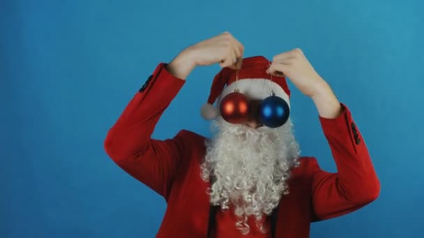 New year, man like a Santa with red and blue Christmas balls baubles toys, on blue background - Footage, Video