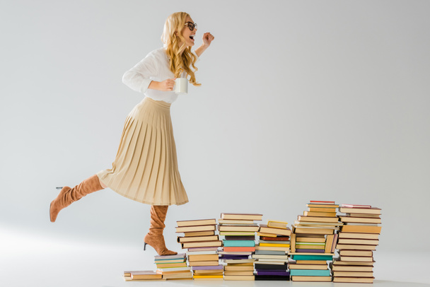 adult stylish woman standing on books with white mug  - Foto, Imagem