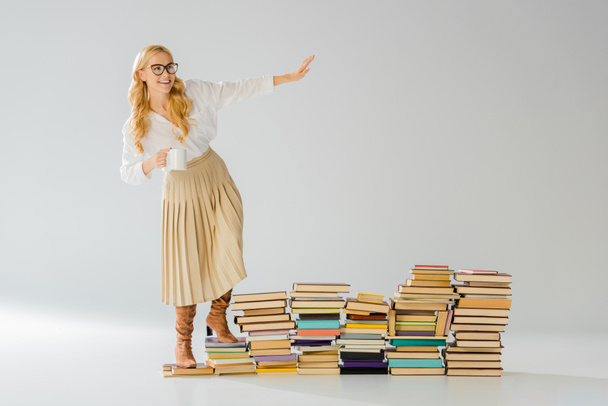 adult stylish woman standing on books with white mug  - Foto, afbeelding