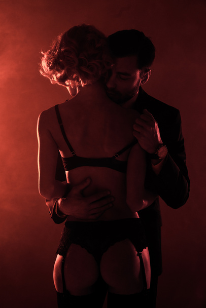 Homem abraçando o homem sedutor em lingerie maravilhosa no fundo de fumaça vermelha
 - Foto, Imagem