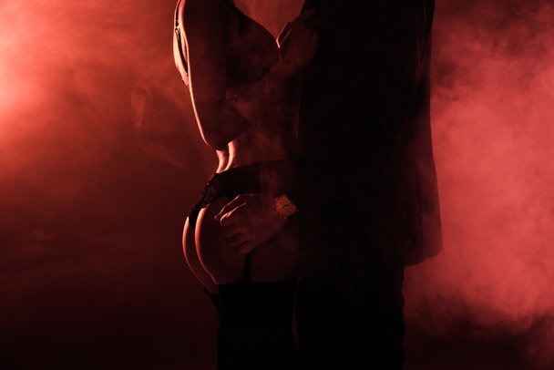 Partial view of attractive seductive couple in hug on red smoke background - Photo, Image