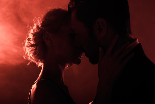 Szinte, kissing, vörös füst háttérben vonzó fiatal pár - Fotó, kép