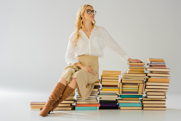 beautiful blonde woman in glasses sitting on pile of retro books - Фото, изображение
