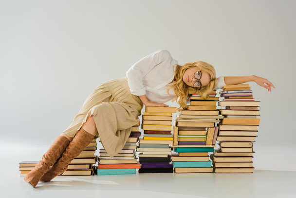 tired blonde woman in glasses laying on pile of retro books - Foto, afbeelding