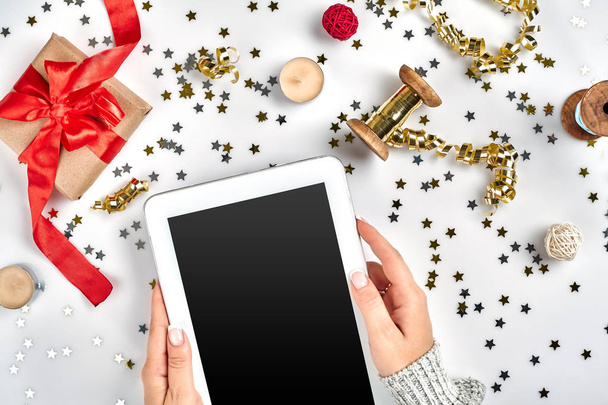 Плоский простір, різдвяна композиція зверху на білому тлі. Цифровий планшет, подарункова коробка з червоною стрічкою, спіральна стрічка, золотий бісер, зірки конфетті
. - Фото, зображення