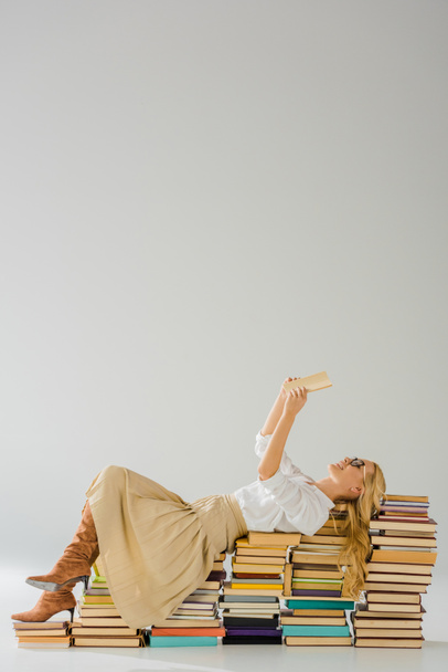 beautiful blonde woman in glasses reading and laying on pile of retro books - Fotoğraf, Görsel