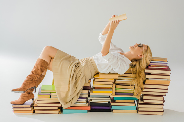 όμορφη ξανθιά γυναίκα γυαλιά ανάγνωσης και τοποθέτηση πασσάλων ρετρό βιβλία - Φωτογραφία, εικόνα