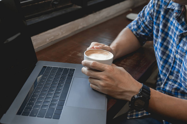 Geschäftsmann trinkt Kaffee in Tasse, während er am Laptop arbeitet. Nahaufnahme Hand hält Kaffeetasse bei der Arbeit. - Foto, Bild